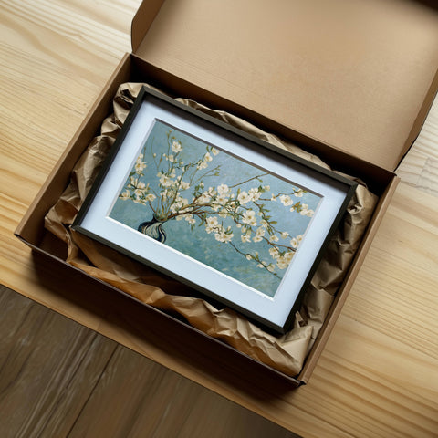 一幅梵谷《杏花盛開》風格的藝術微噴畫作,裝裱於白框內,精緻地擺放在牛皮紙盒與包材中,展現溫暖陽光下藝術品開箱的細膩質感,非常適合送禮或收藏。